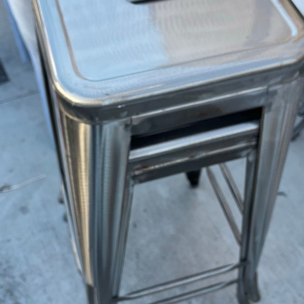 1. Close-up of two stacked metal stools with a brushed steel finish on a concrete floor.