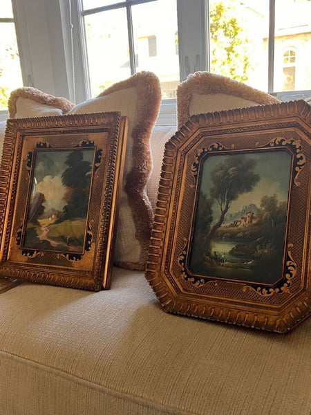 1. Two ornate gold-framed landscape paintings resting on a cream sofa with decorative pillows behind them.