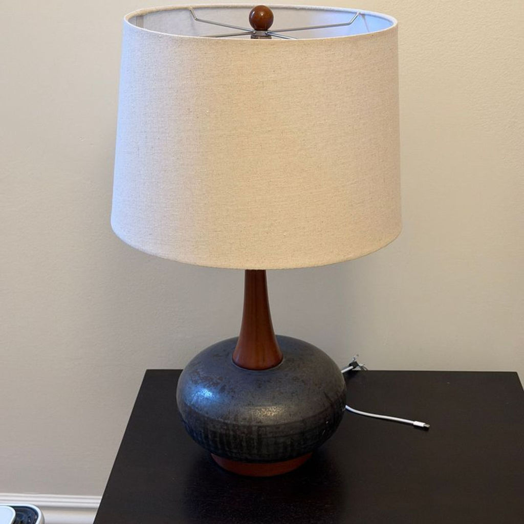 1. Table lamp with beige drum shade, wooden neck, and dark ceramic base on a black surface.