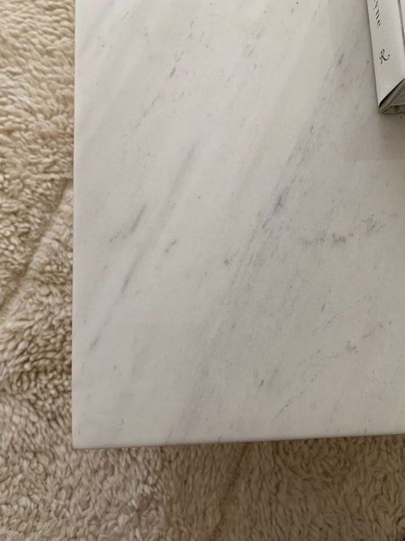 1. Close-up of a white marble Rove Concepts coffee table on a textured beige rug, showing a book in the corner.