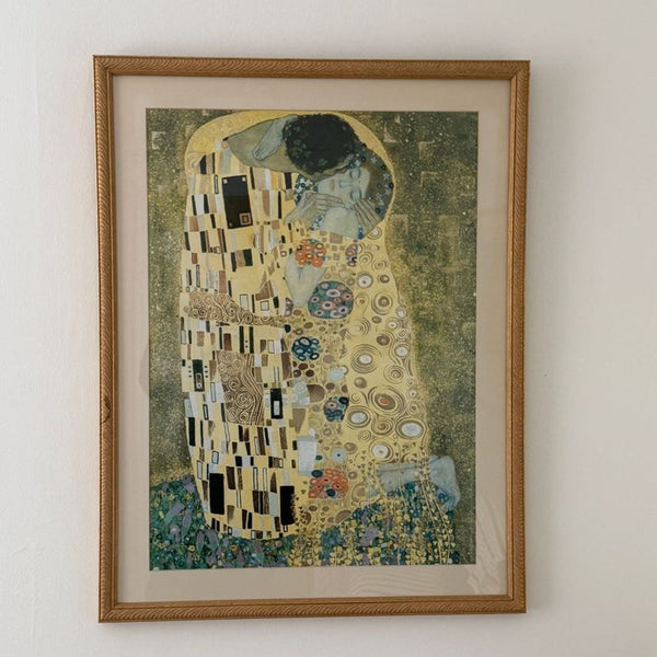 Framed print of Gustav Klimt’s "The Kiss" hanging on a light-colored wall, under glass.  