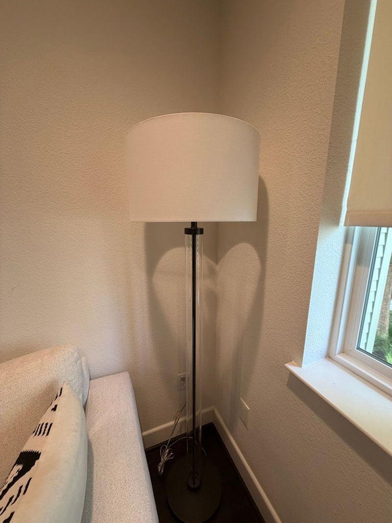 1. Arhaus floor lamp with white drum shade and slim clear stand, placed beside a sofa and window.  