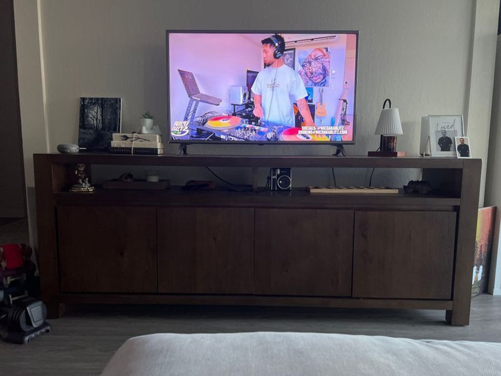 2. Brown Living Spaces TV stand with shelving and cabinets, holding a flat-screen TV and various personal items.