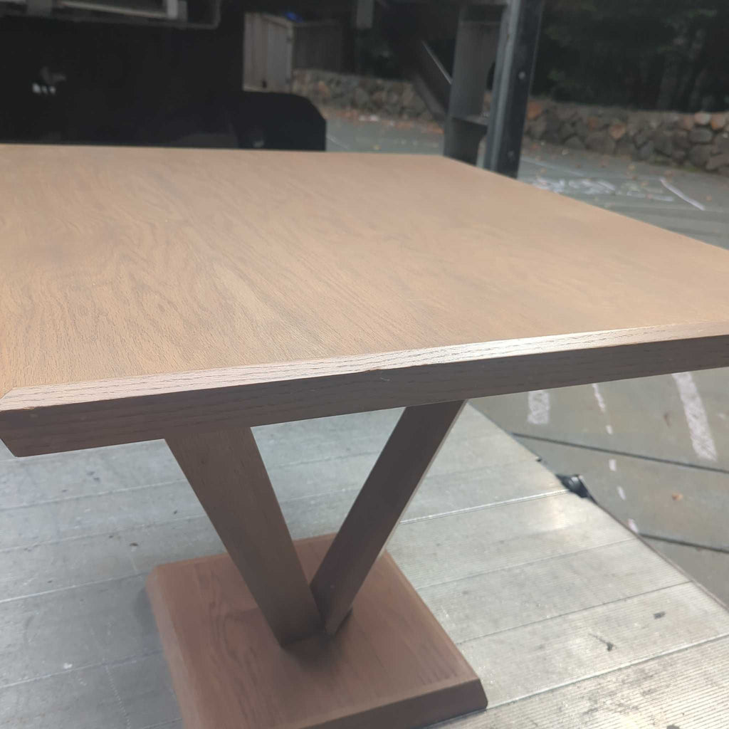 1. Modern wooden dining table with a square top and unique V-shaped base, placed outdoors on a wooden platform.