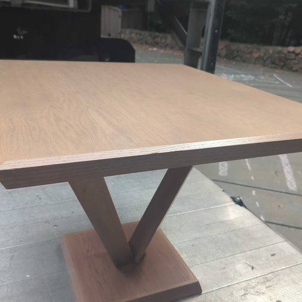 1. Modern wooden dining table with a square top and unique V-shaped base, placed outdoors on a wooden platform.