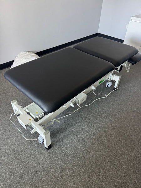 1. Adjustable black and white MedSurface exam table, positioned flat in a clinical setting with gray flooring.