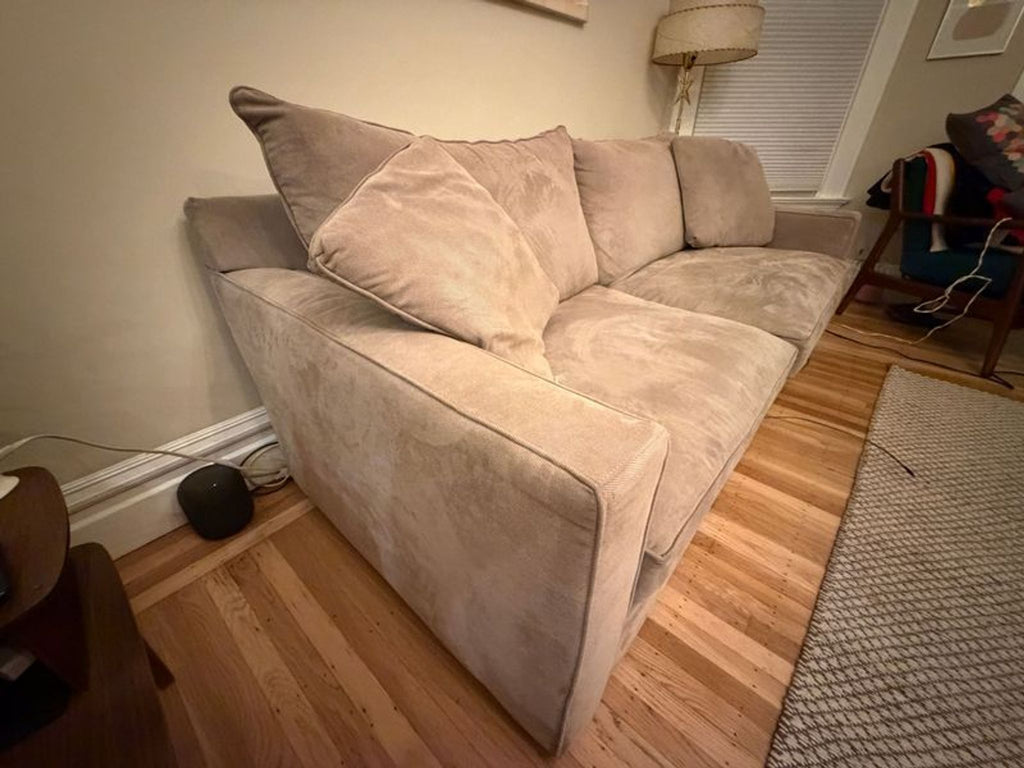 1. Beige Room & Board sleeper sofa with plush cushions, angled view in a cozy living room with wood floors.