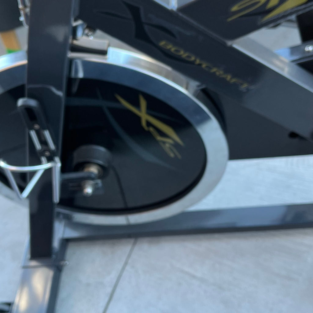 Close-up of a BodyCraft exercise bike flywheel and frame, gym equipment on a concrete floor.  