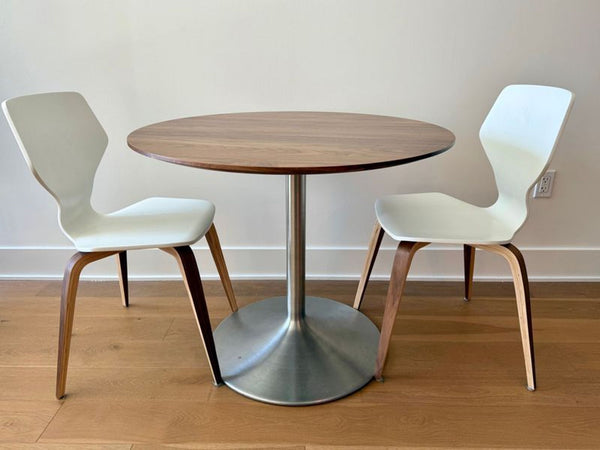 Round walnut dining table with aluminum base, paired with two wood chairs, shown as a dining set.