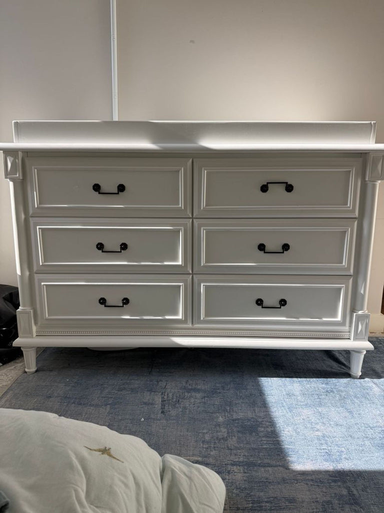 1. White Simmons Juvenile Furniture dresser with six drawers and black handles, shown in natural light on a blue rug.  