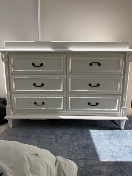 1. White Simmons Juvenile Furniture dresser with six drawers and black handles, shown in natural light on a blue rug.  