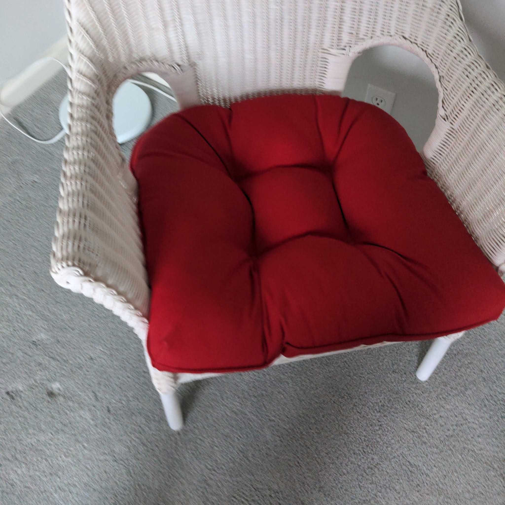 2. White wicker lounge chair with a thick, tufted red cushion on the seat, placed on carpeted flooring.
