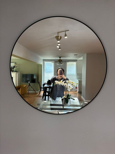 1. Round Ikea mirror with a thin black frame, reflecting a modern living room interior and dining area.