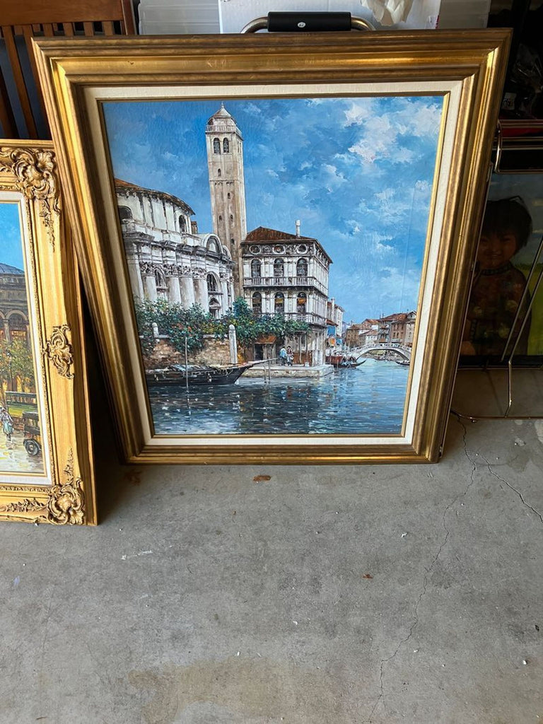 1. Framed oil painting of a canal scene with historic architecture, blue sky, and water reflections, in gold frame.