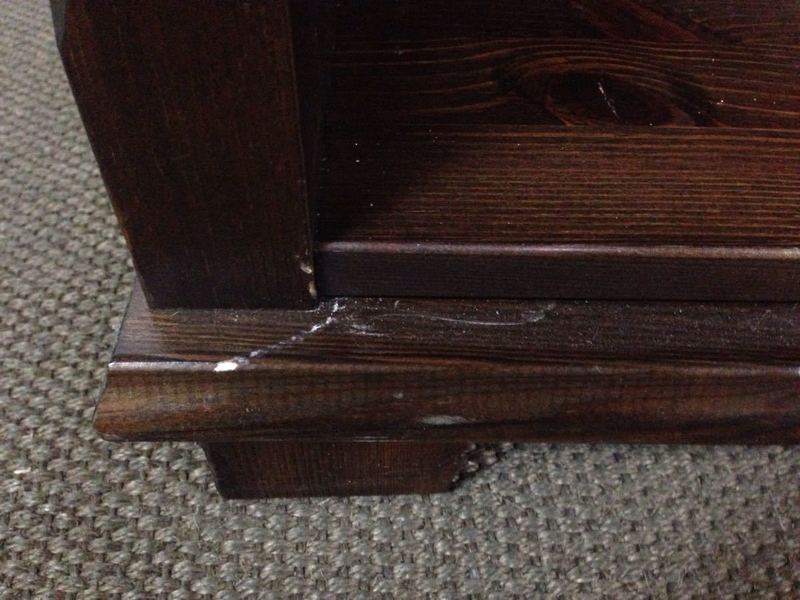 3. Detail of lower corner of dark brown bookshelf, showing wood grain and minor wear marks.