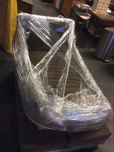 1. Crate & Barrel sofa wrapped in plastic, ready for delivery or storage in a dimly lit room.