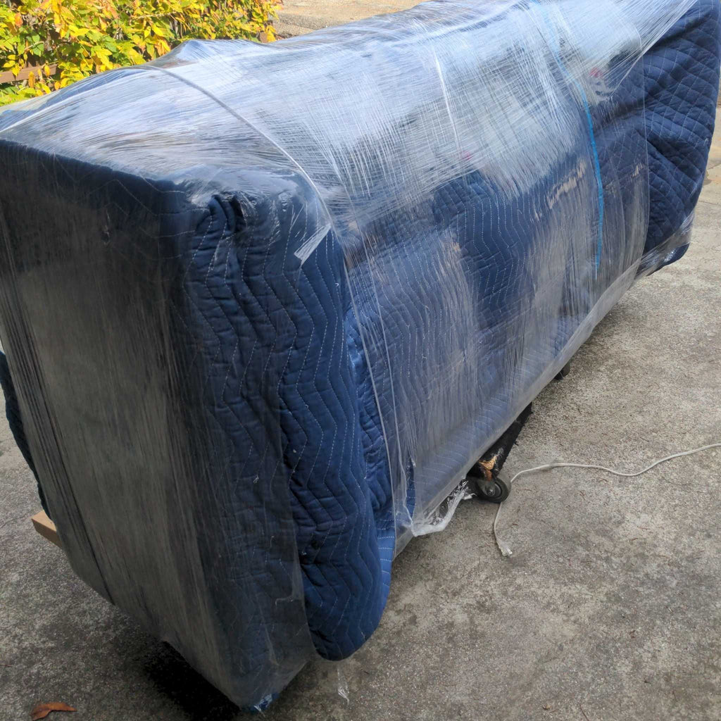 3. Reperch 3-seat sofa fully wrapped in blue moving blankets and plastic, placed on a dolly outdoors.