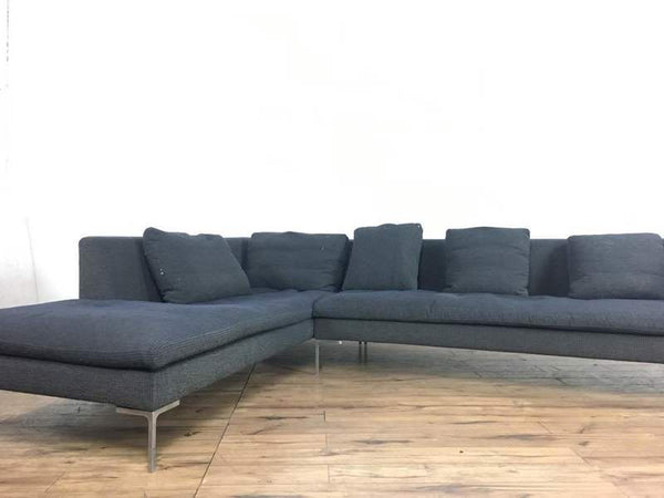 Dark gray sectional sofa with metal legs by B&B Italia, shown in a bright room with wood floors.  