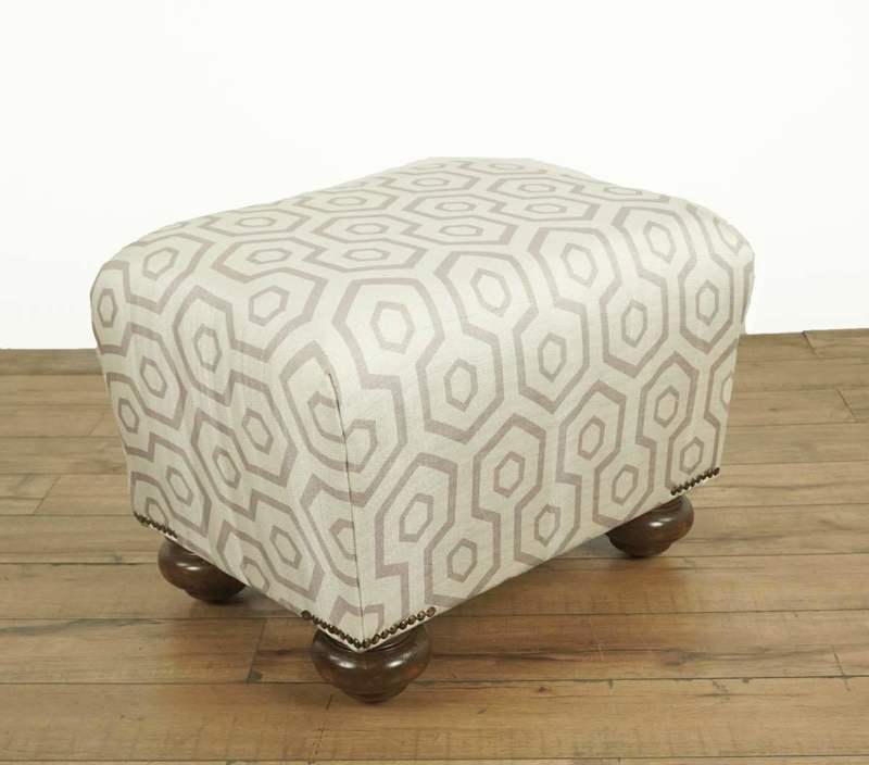 Silk blend upholstered ottoman with a geometric keyhole pattern and bun form wooden legs on a wood floor.