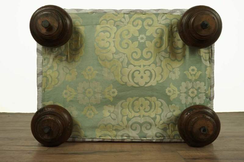 Bottom view of ottoman showing light green floral-patterned base fabric and four dark wooden bun legs.