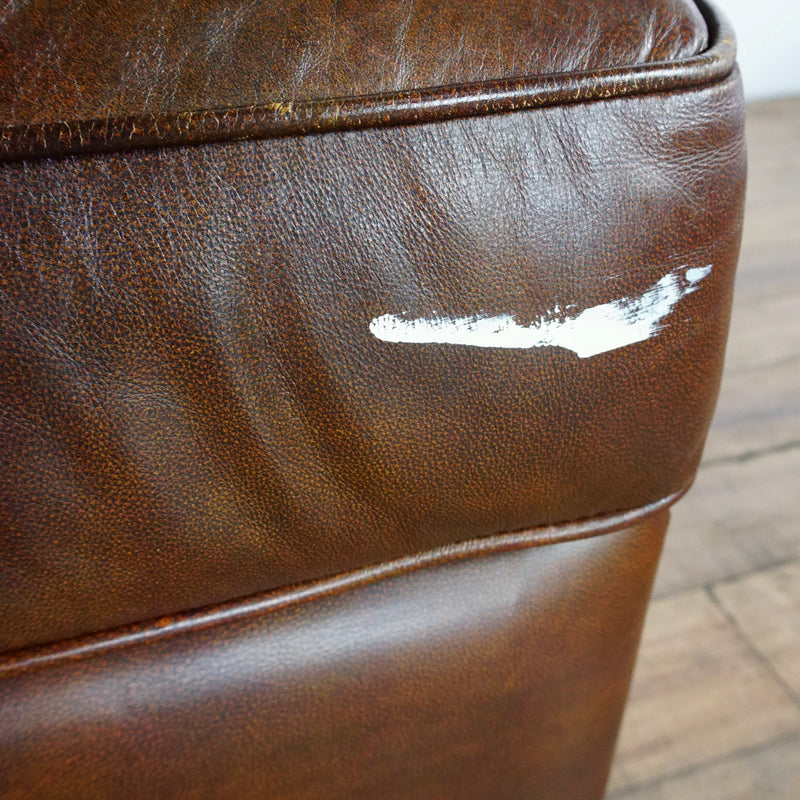 3. Close-up of a white paint streak on the rim of a Lane Furniture brown leather chair cushion.