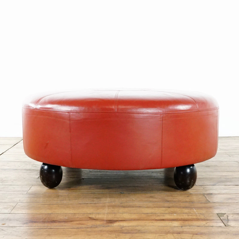 2. Side view of a Reperch red leather ottoman, showing wooden bearing legs and stitched detail.  