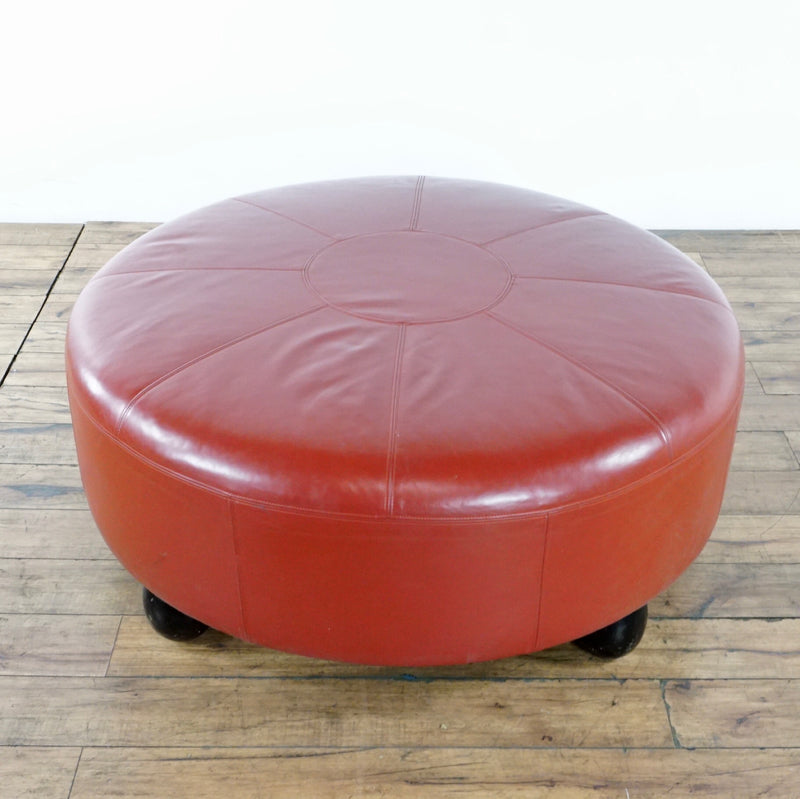 1. Large round custom-made red leather ottoman with bearing wood legs, by Reperch, on wooden floor.  