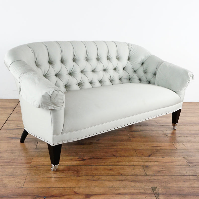 2. Reperch brand tufted back sofa in pale upholstery, featuring exposed nailhead trim and wood legs with casters.  