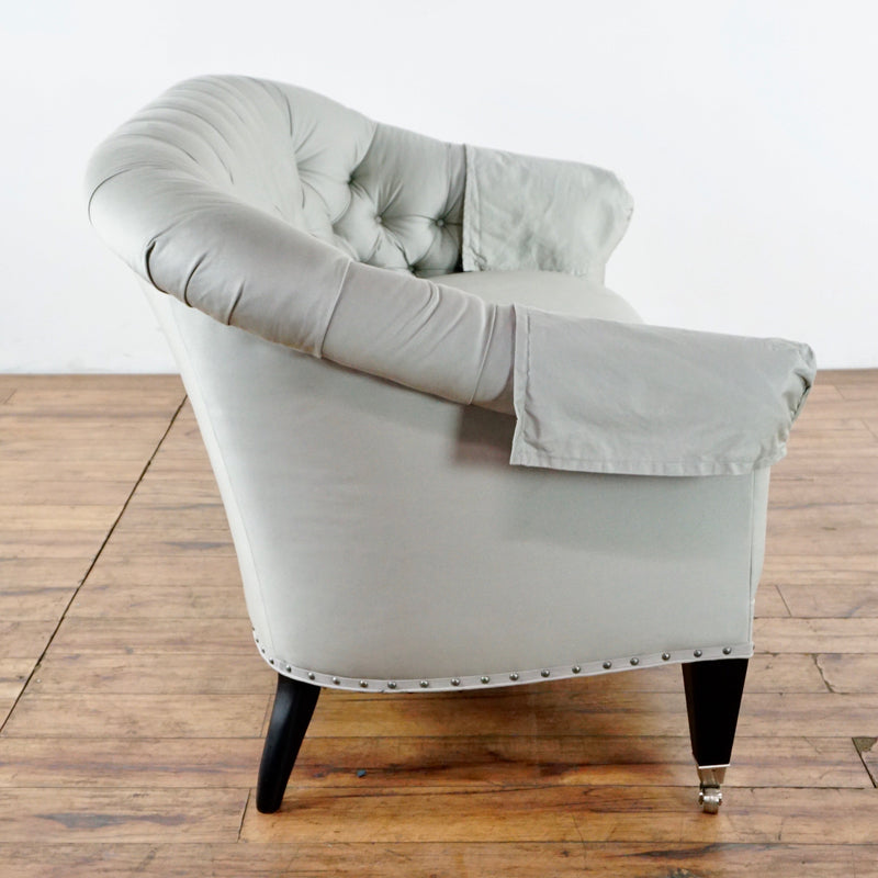 3. Side view of a Reperch sofa with rolled arms, nailhead trim, tufted back, and wood legs on casters.