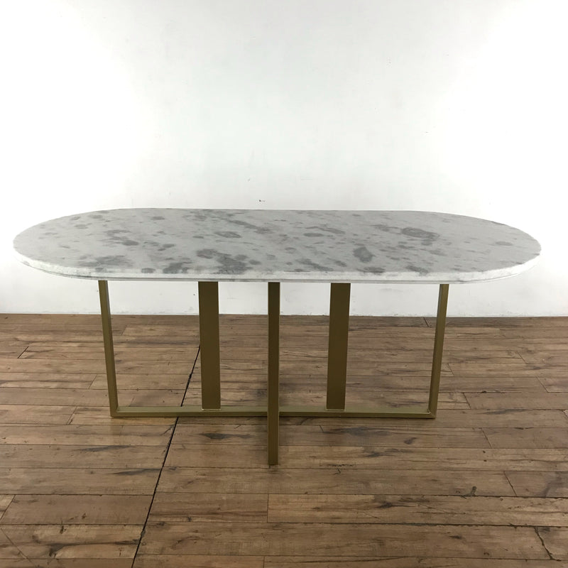 2. Close-up of Dylia dining table featuring an oval marble top and brass-finished iron base on wooden floor.