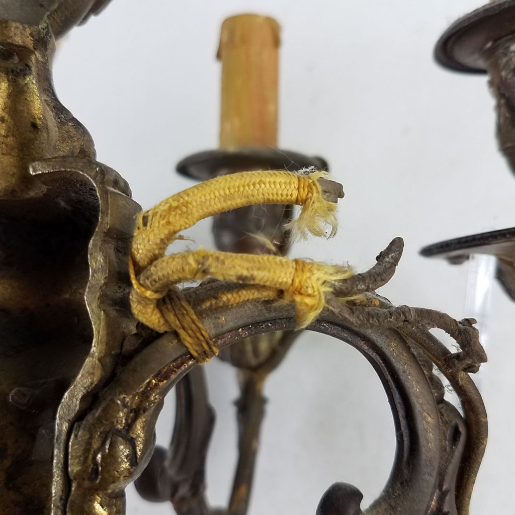 Close-up of vintage bronze sconce arm showing aged patina and original fabric-wrapped electrical wiring.  