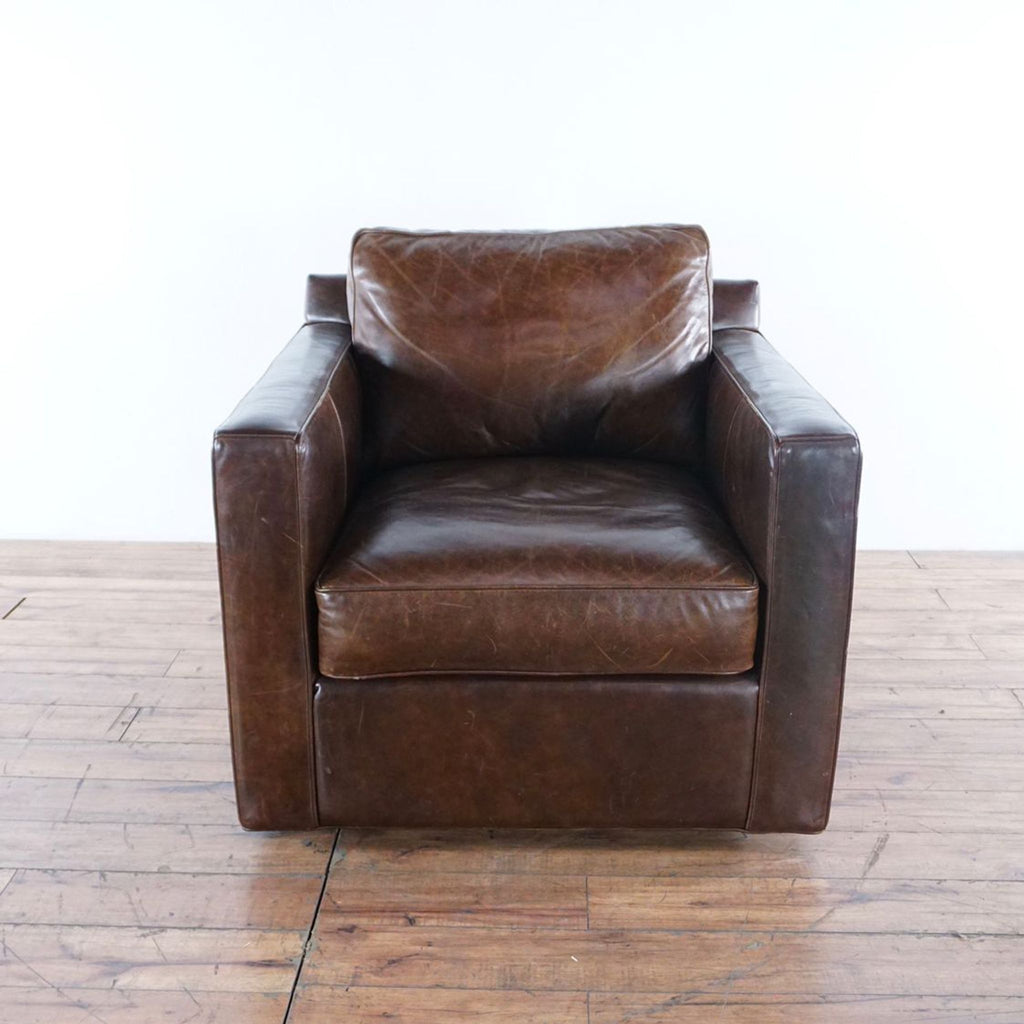 1. Front view of a Crate & Barrel brown leather swivel chair with boxy arms and plush cushioning on wooden flooring.