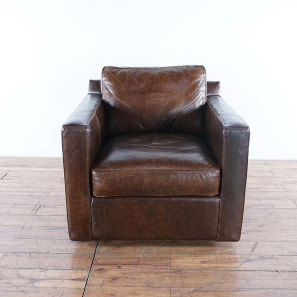 1. Front view of a Crate & Barrel brown leather swivel chair with boxy arms and plush cushioning on wooden flooring.