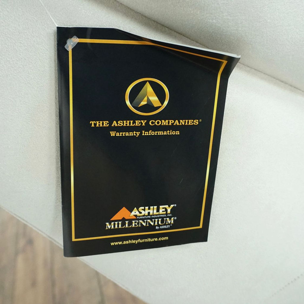 2. Close-up of original Ashley Furniture Millennium label and warranty information attached to the sofa.