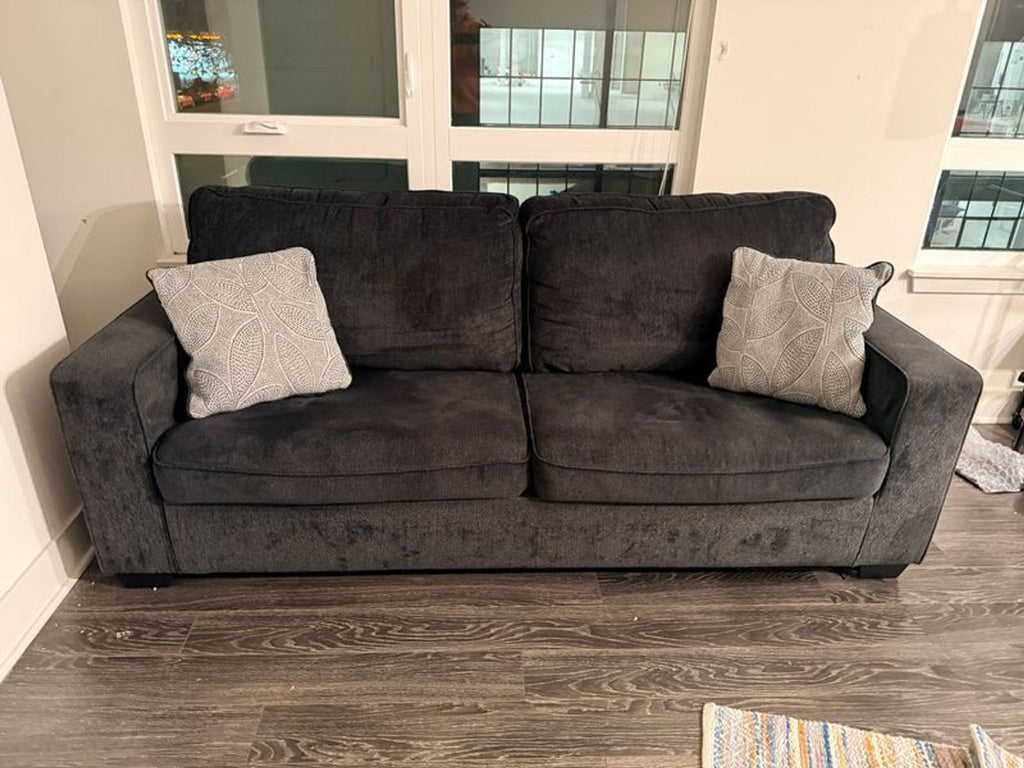 2. Ashley Furniture dark gray sleeper sofa, shown from the front, with two decorative pillows and wood flooring.