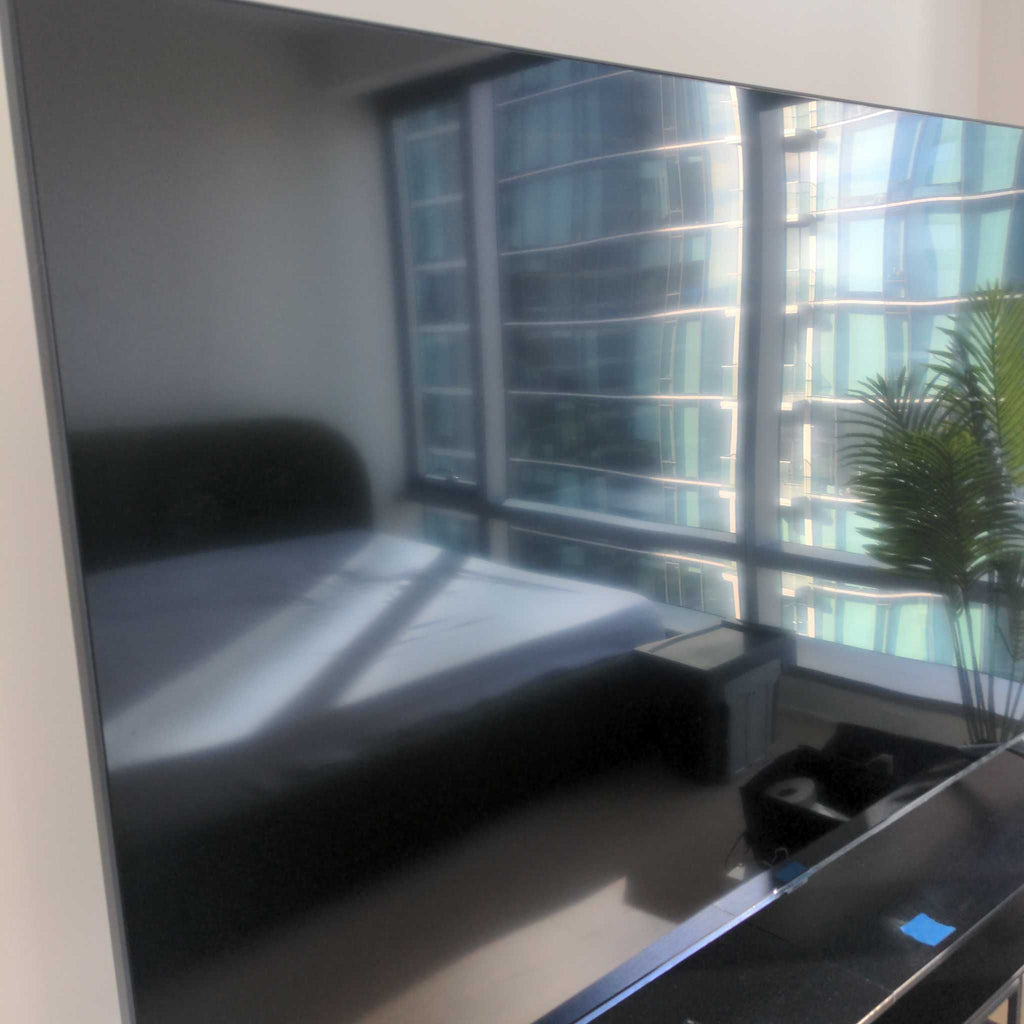 Reperch TV with a dark screen reflecting a bright bedroom and windows with city views, plant visible beside.