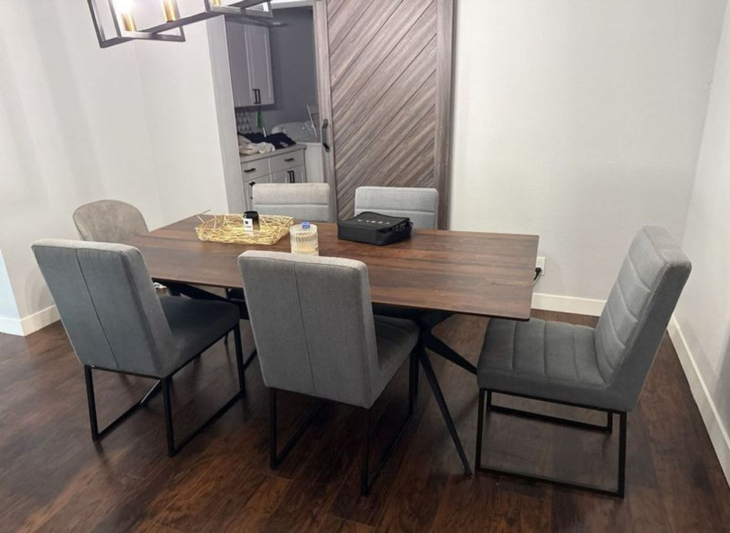 Modern dining table with a dark wood top, black metal legs, and six gray padded chairs in a minimalist room.  