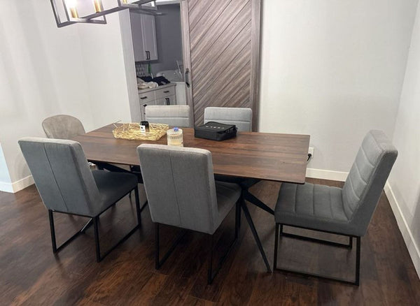 Modern dining table with a dark wood top, black metal legs, and six gray padded chairs in a minimalist room.  