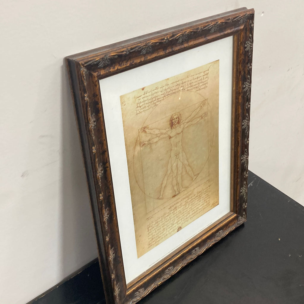 2. Angled view of framed Reperch Vitruvian Man artwork, classic brown frame, displayed on a black surface.