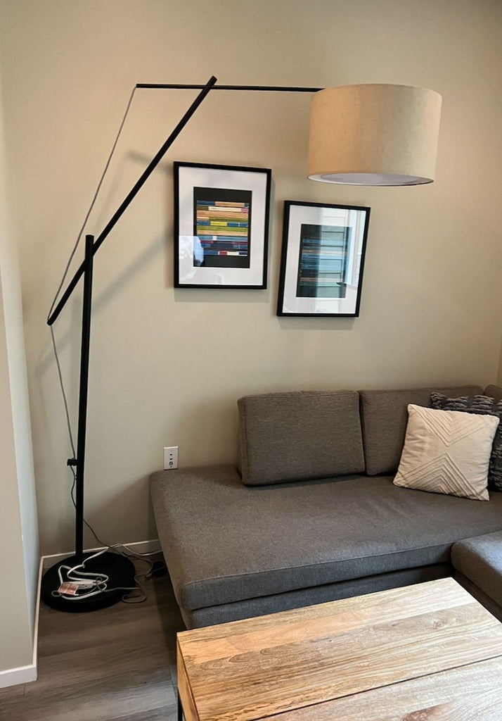 Reperch lamp with angled arm and beige shade placed in a cozy living room next to a sofa.