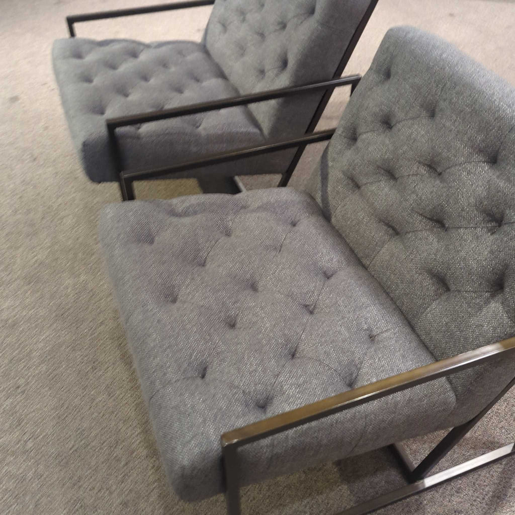 2. Side angle of Alder & Tweed lounge chairs featuring grey tufted cushions and sleek metal armrests.
