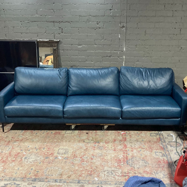 1. Blue 3-seat sofa with sleek lines, set against a gray brick wall on a patterned rug.