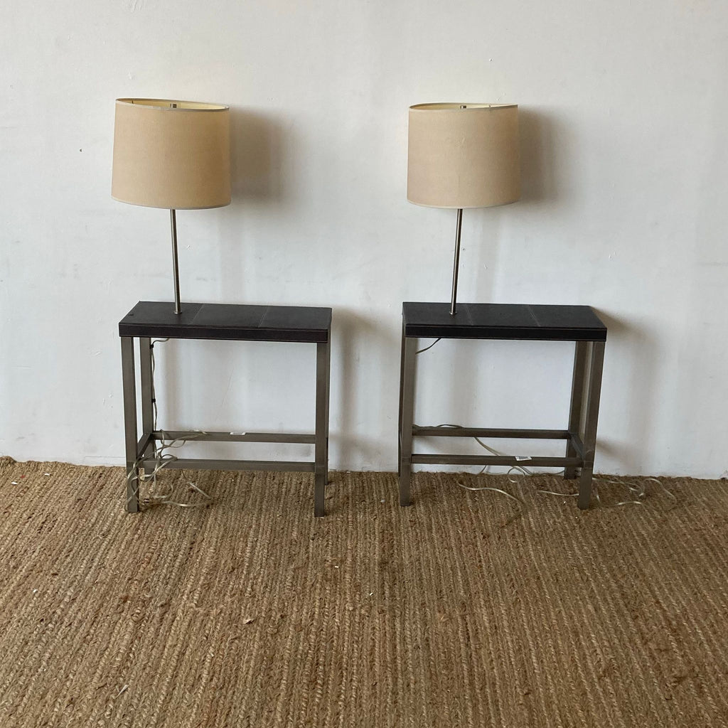 End tables with lamps on woven rug, white wall background.