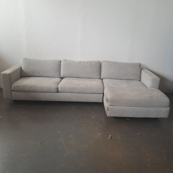Light gray Design Within Reach sectional sofa with right chaise, shown against a plain wall on a concrete floor.