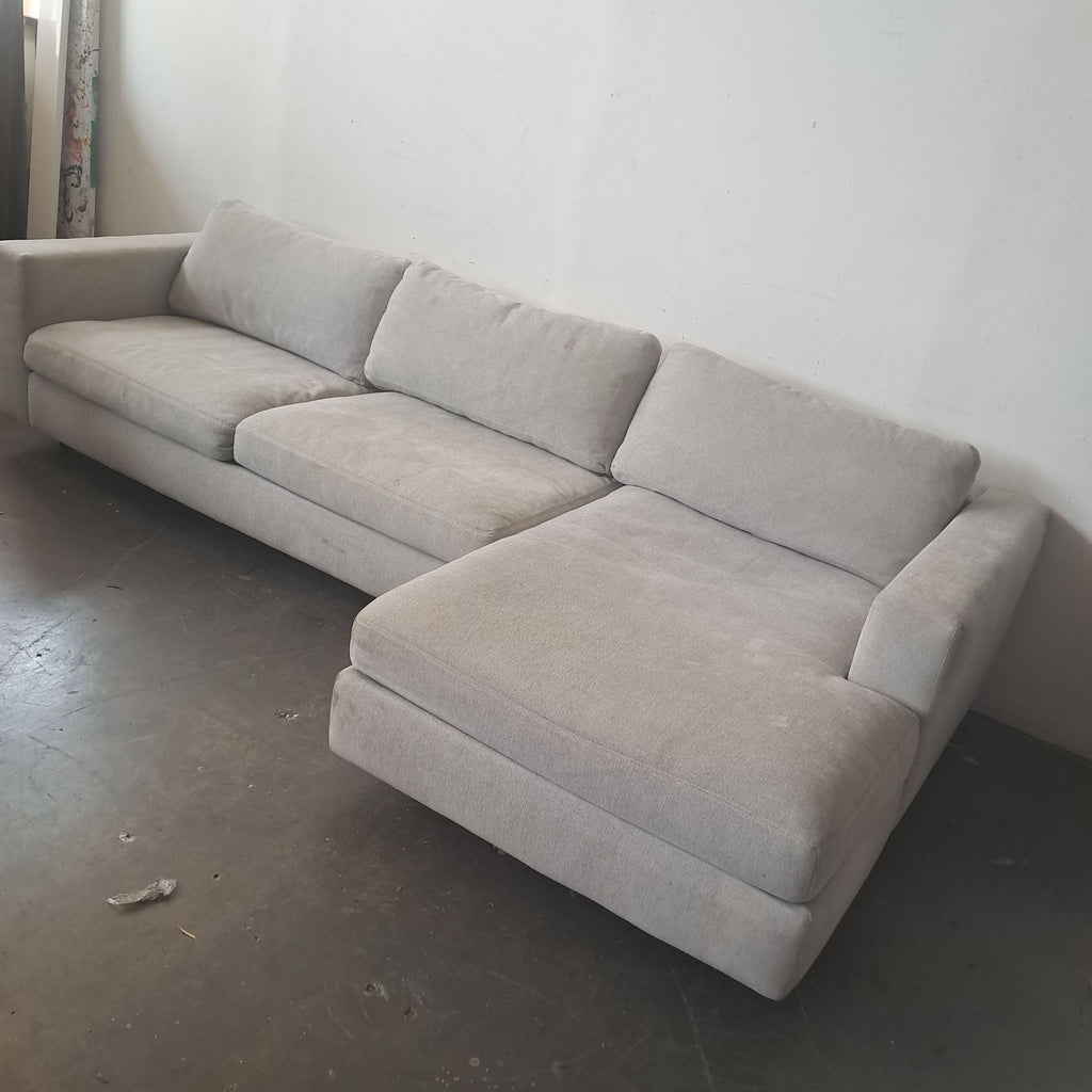 Angled view of a light gray Design Within Reach sectional sofa, featuring modern lines and a deep right chaise.
