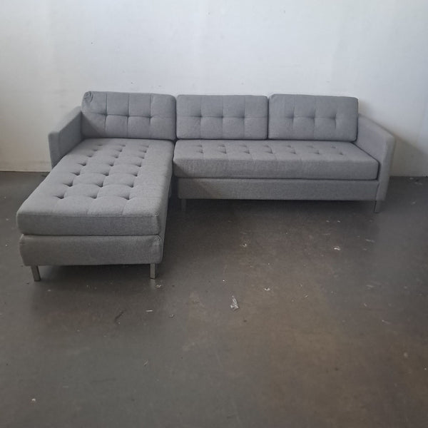 1. Grey CB2 sectional sofa with tufted cushions, set against a plain wall, 98" W x 74" D x 30" H.
