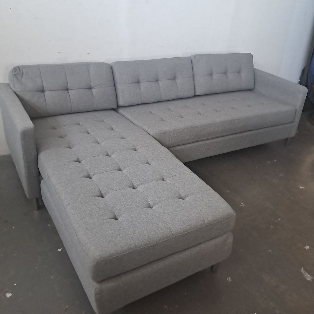 2. Modern CB2 sectional in light gray fabric, featuring tufted seats and clean lines, shown from an angle.