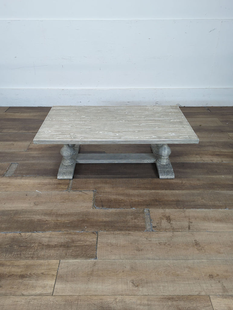 3. Wide wood grain Reperch coffee table with carved pedestal legs, pictured from the front on a wooden surface.