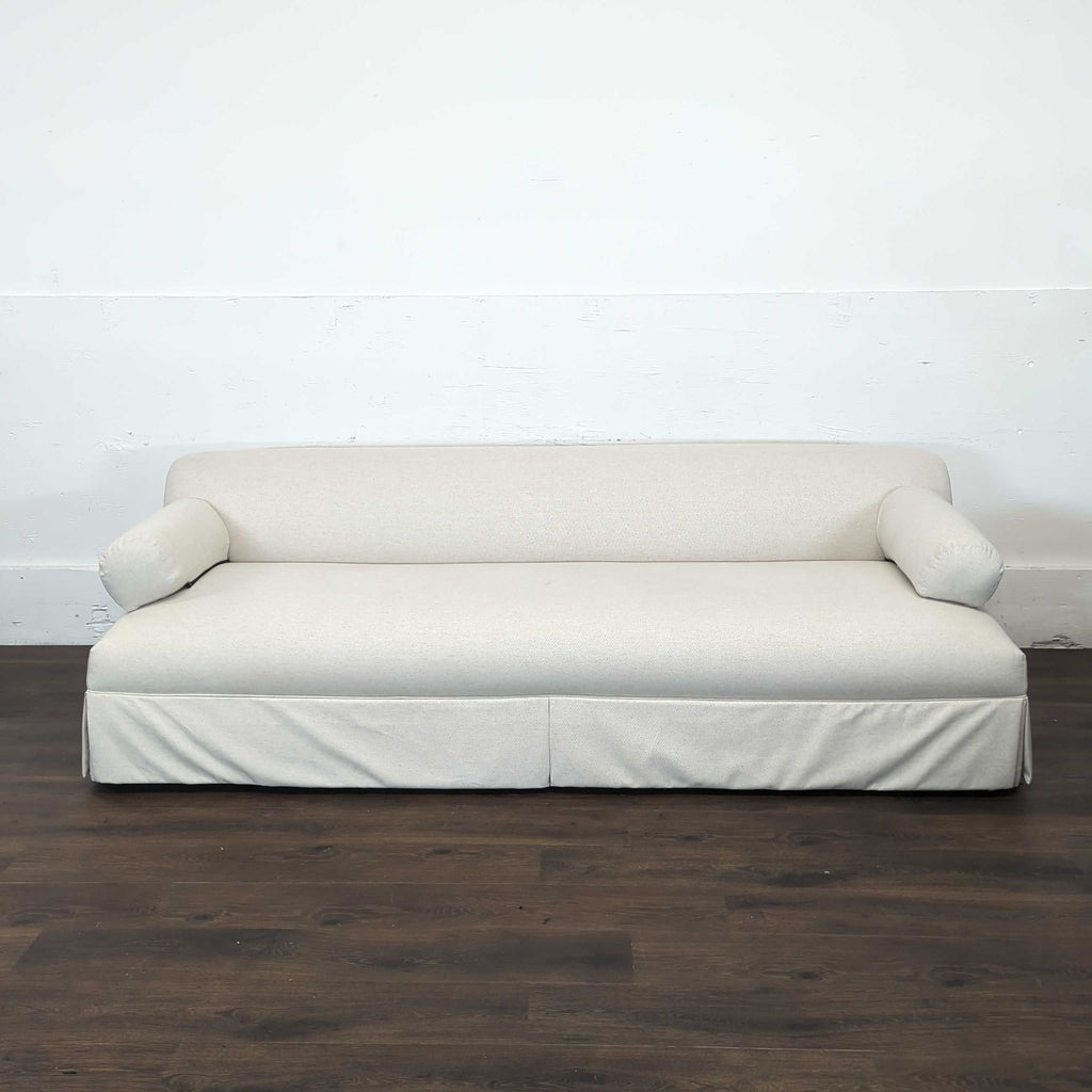 1. Front view of a Shoppe Amber Interiors 3-seat sofa in light beige with bolster pillows and skirted base.