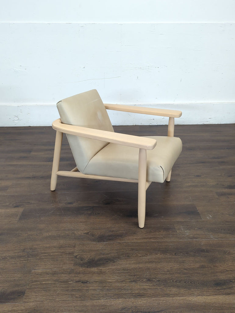 2. Modern Four Hands tan leather lounge chair with pale wood arms, placed on a dark wood floor, angled view.